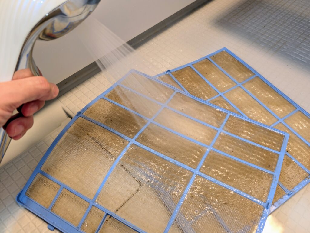 埃やカビがついたエアコンフィルターを掃除する様子
