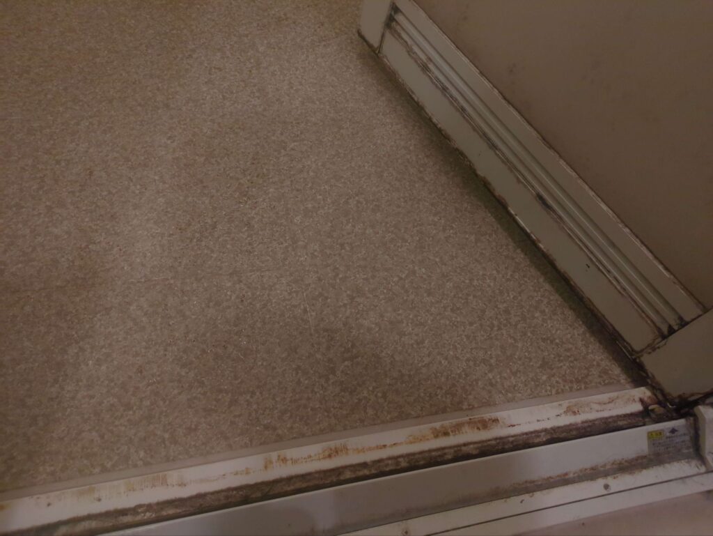 横浜市戸塚区で浴室クリーニングを行う前の、頑固な水垢がびっしりこびりついた浴室扉の様子